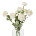 Pale cream artificial flowers with layered rounded blooms and green foliage, shown as a multi-stem arrangement in a clear vase against white.