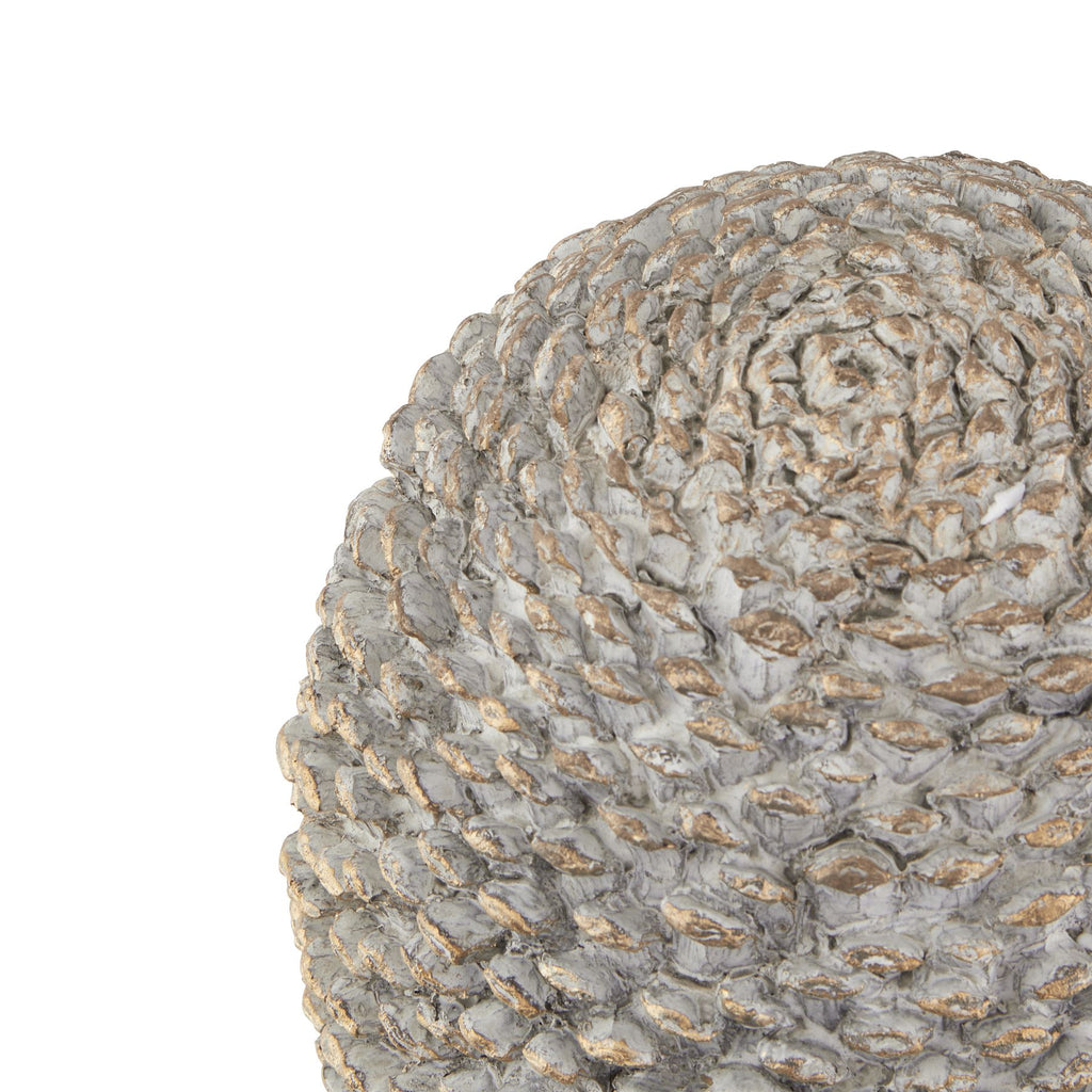 Close-up of the pinecone ornament's rounded top, showing overlapping grey-white scales with warm golden edges.