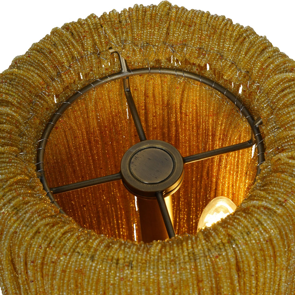 View into the open top of the lamp, showing amber beads draped over a circular metal frame and a lit bulb inside.