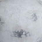 Close-up of the vase's layered pale surface, showing uneven texture and scattered dark grey patches.