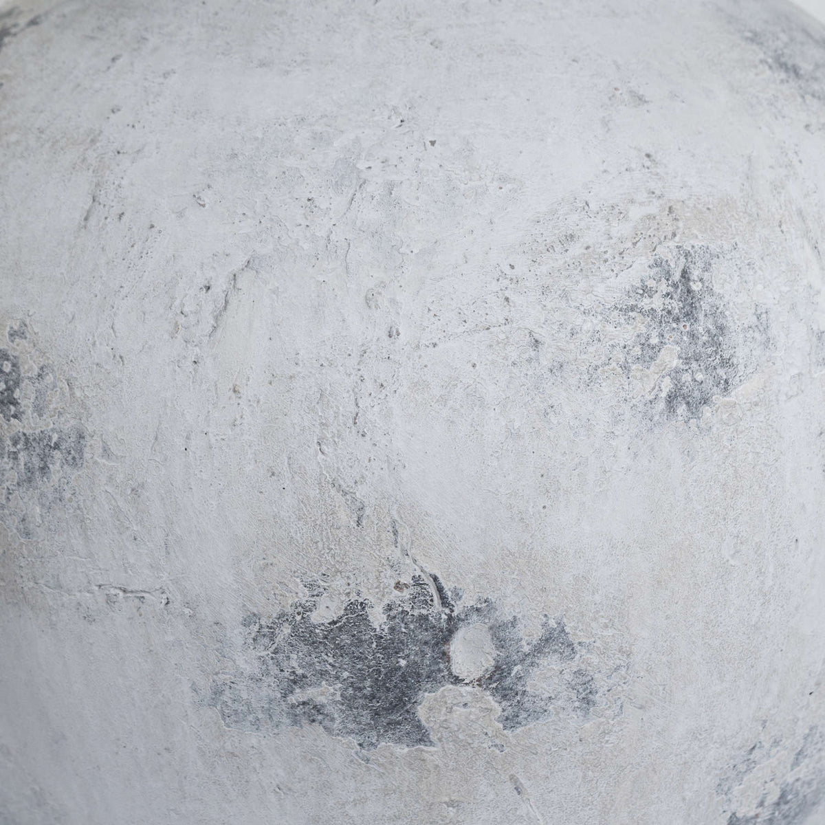 Close-up of the vase's layered pale surface, showing uneven texture and scattered dark grey patches.