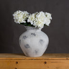 White and grey rounded vase styled with white hydrangea blooms on a wooden sideboard against a dark wall.