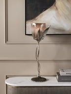 Leaf Stem Hurricane holding a lit candle on a pale console beside stacked books, beneath an abstract painting.