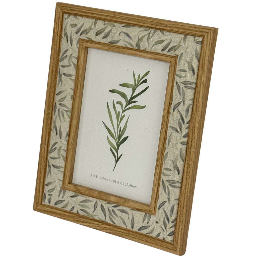 Angled view of the photo frame showing its warm wood-tone edges and scattered grey-green leaf pattern around a botanical display insert.