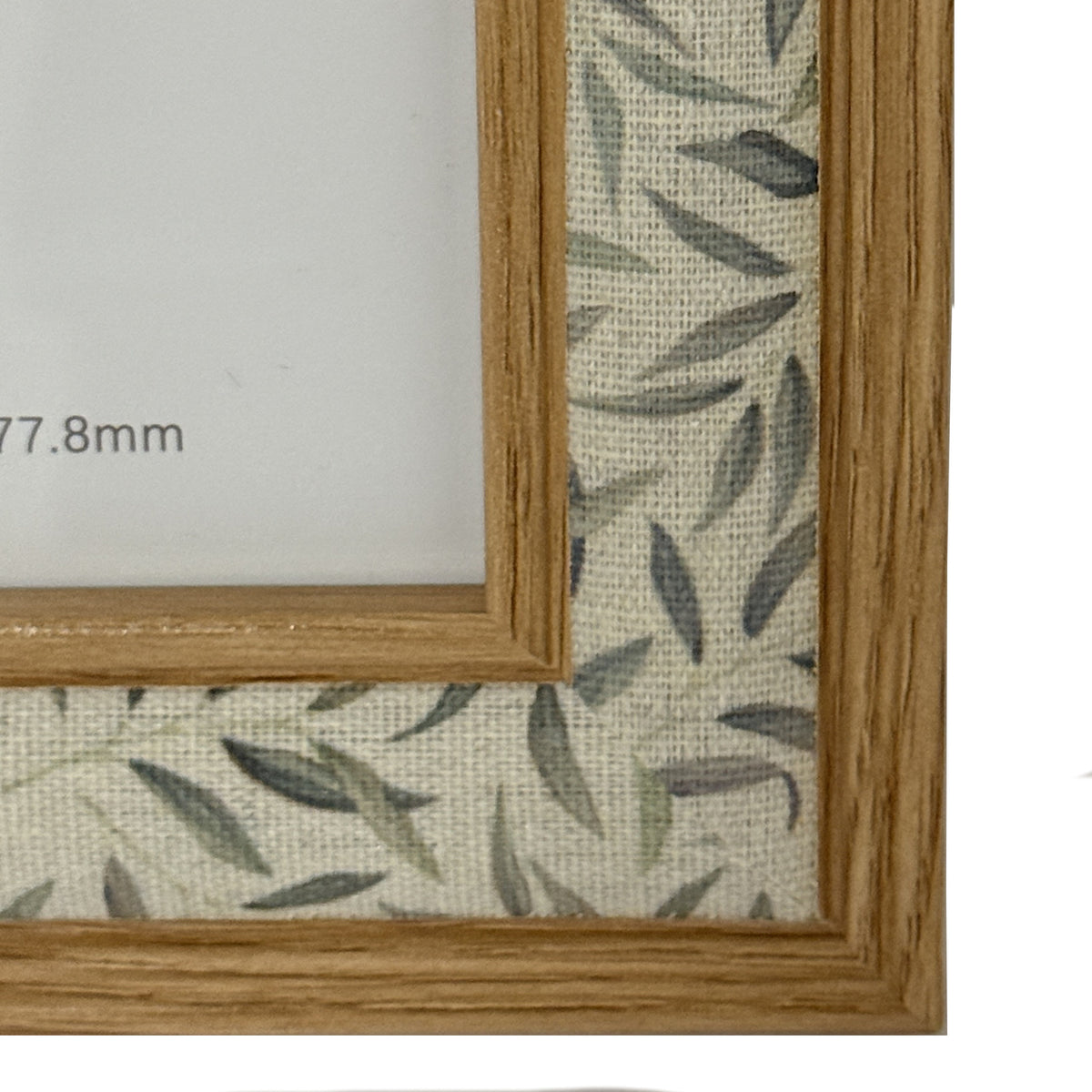 Close-up of the frame's lower right corner, showing grain-like lines on both trims and the textile-like texture beneath the leaf print.