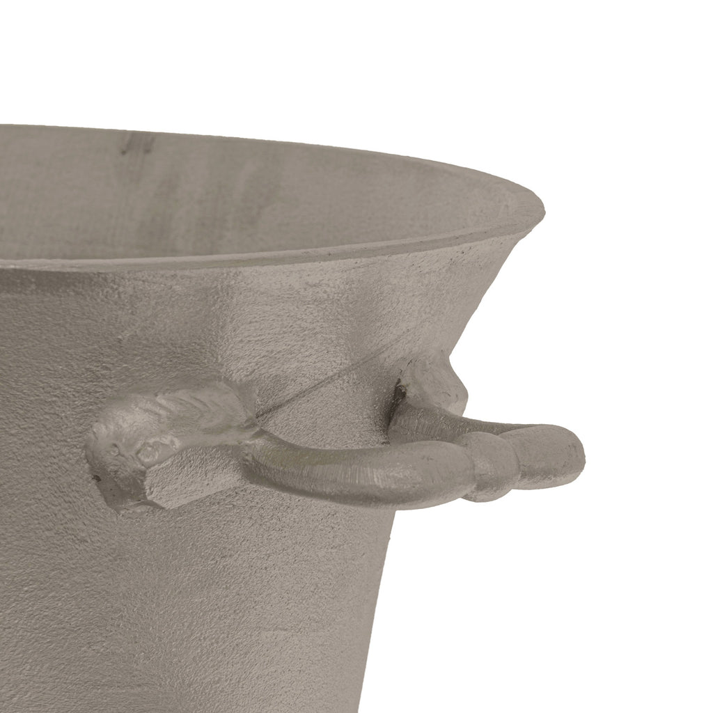 Close-up of a rounded side loop handle, flared rim and textured silver-coloured surface of the oval champagne cooler against white.
