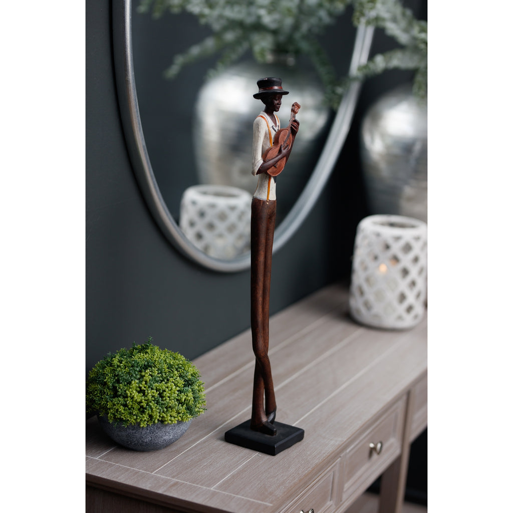 Angled view of the guitarist figurine on a pale wooden console beside a potted plant, with an oval mirror and white lattice lantern behind.
