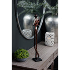 Full-length front three-quarter view of the guitarist figurine on a console, showing its crossed legs and dark base beside greenery and a white lantern.