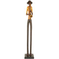 Standing saxophonist figurine with very long legs, a yellow shirt, reddish braces and a dark brimmed hat, on a rectangular plinth against white.