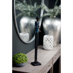 Musician figurine displayed on a pale wood console beside a small green plant, with a round mirror, white lantern and silver-toned vase behind.