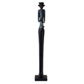 Full-length view of a slender musician figurine with a tall dark hat, blue shirt, reddish braces and long black legs, playing a straight wind instrument on a dark rectangular plinth.