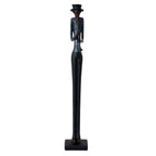 Full-length view of a slender musician figurine with a tall dark hat, blue shirt, reddish braces and long black legs, playing a straight wind instrument on a dark rectangular plinth.