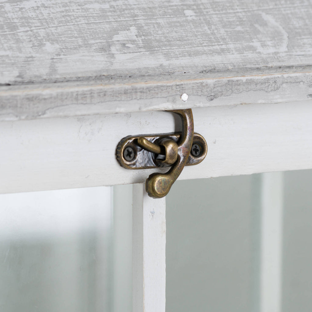 Close-up of the small antique-brass-coloured latch on the white lantern frame beneath the pale roof edge.