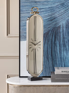 Oval clock displayed on a white-topped console beside stacked books, with a large blue abstract artwork behind it.