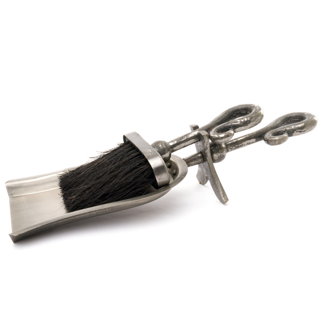 Silver-grey hearth tidy on a white background, with a black-bristled brush resting in a shallow scoop and two open looped stems extending to the right.