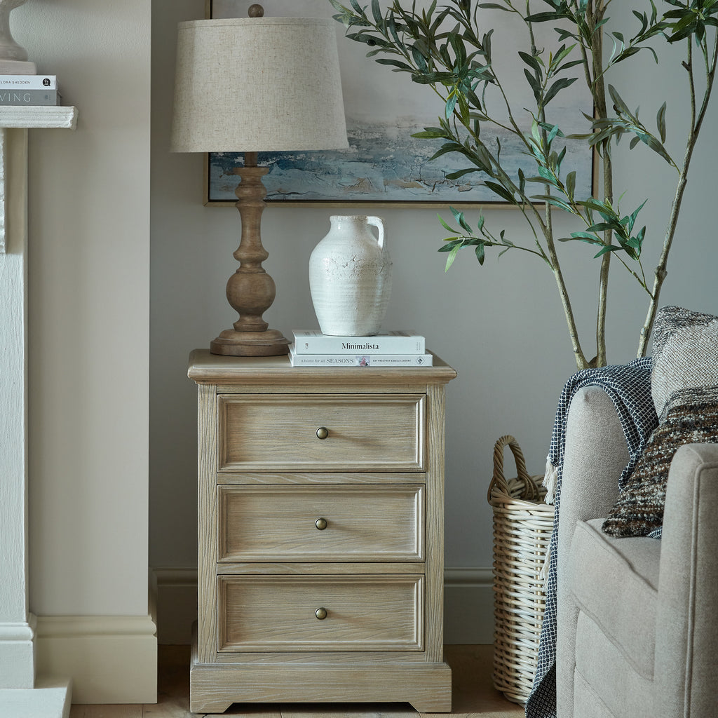 Louvre & Frame chest beside an upholstered armchair, styled with a lamp, books and a pale jug beneath framed artwork.