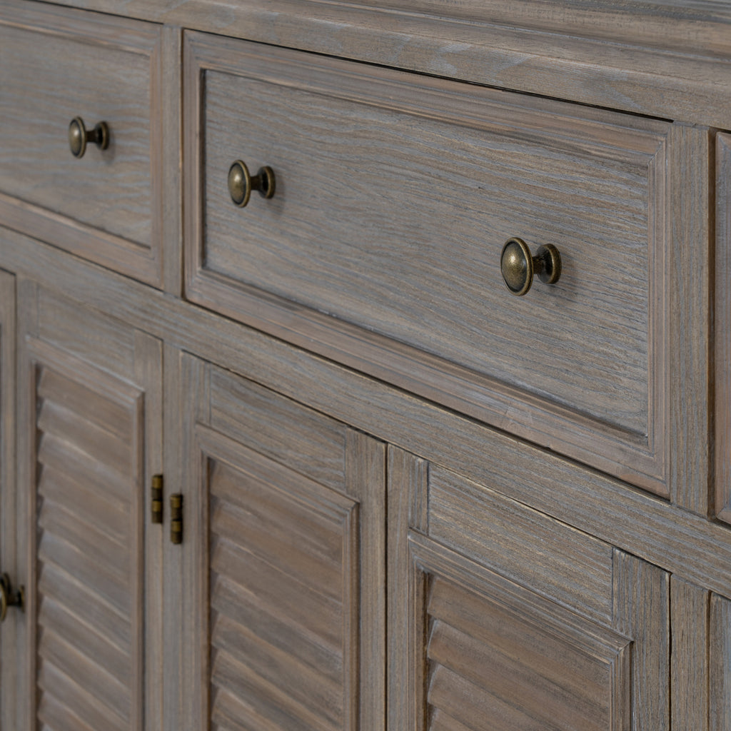 Close-up of a framed drawer front with two dark round knobs and fine grain lines above the louvred doors.