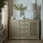 Dresser base styled beneath a large pale artwork with blue-and-white jugs, foliage, books and a table lamp.