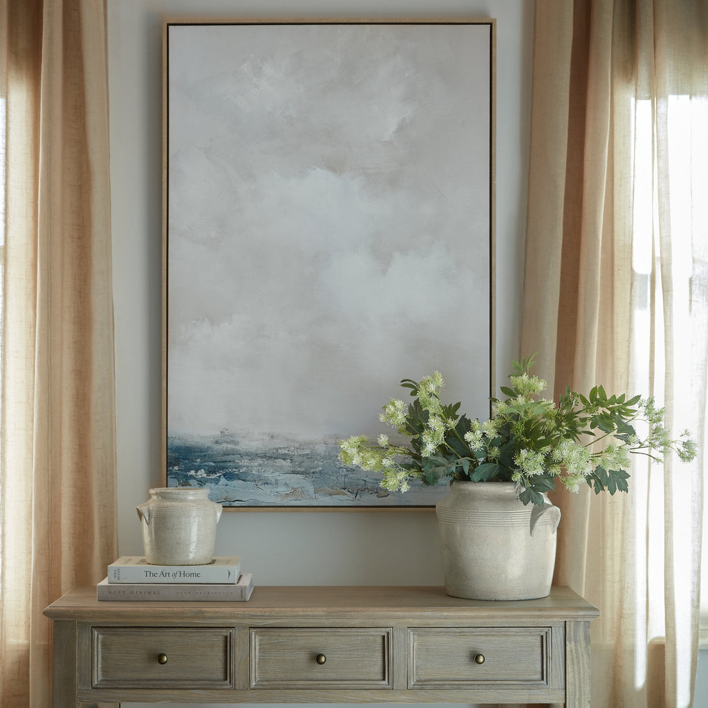Lower Navyfield Framed Artwork above a three-drawer console between beige curtains, styled with books, pale vessels and leafy stems.
