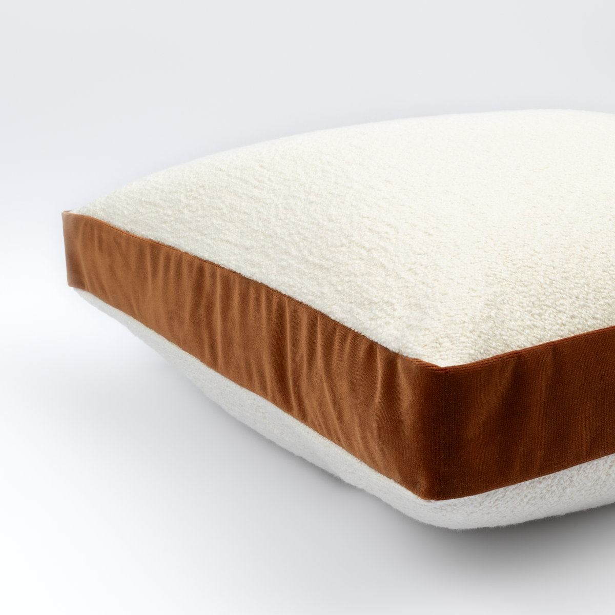 Angled view of the Mirela Bouclé Cushion showing its cream bouclé front and rust velvet band