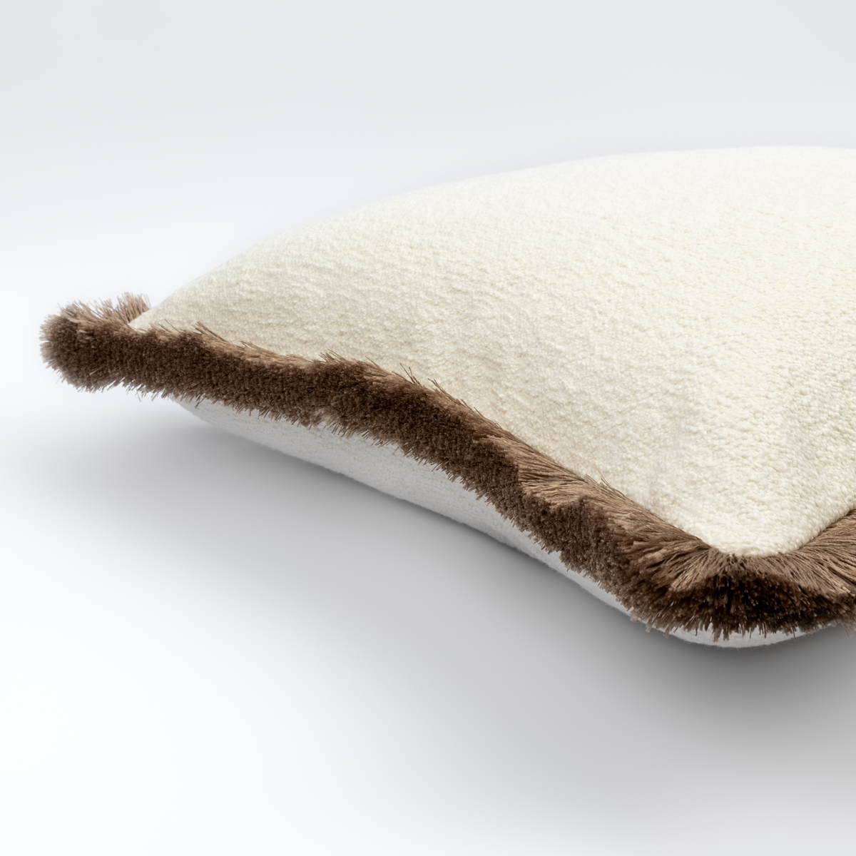 Angled view of the Mirela Bouclé Cushion showing its cream bouclé and mushroom fringe