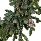 Wreath detail showing a rounded pale-edged pinecone beside overlapping grey-green sprays and brown branching stems with small pink bud-like accents.