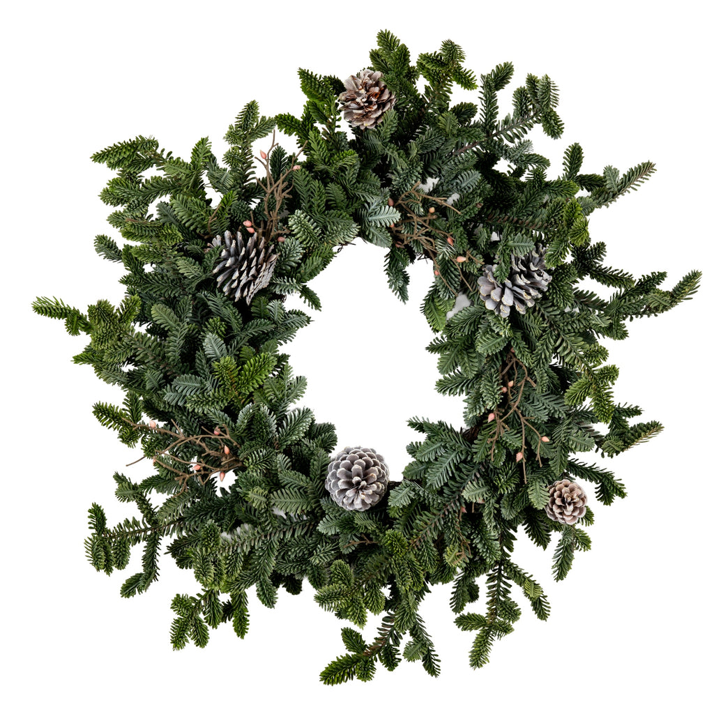 Full view of a circular artificial wreath with an open centre, mixed green fir-like sprays, pale-edged pinecones and small pink-orange accents on white.