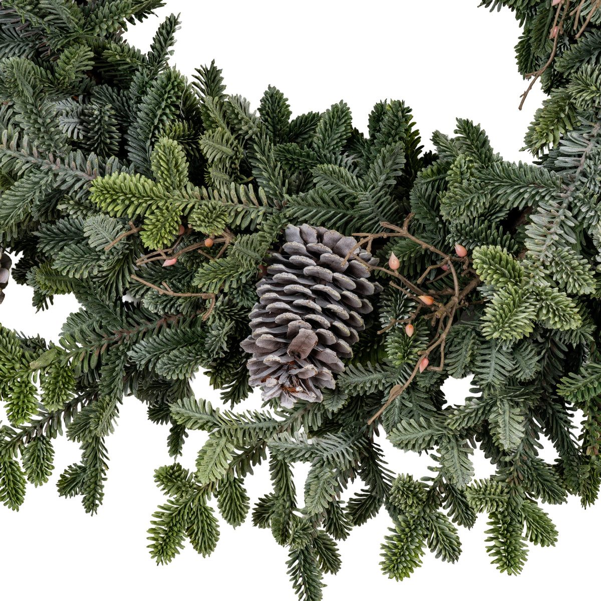 Close-up of an elongated brown-grey pinecone among dense green wreath foliage, with pale scale edges and pink-orange bud-like details on branching stems.