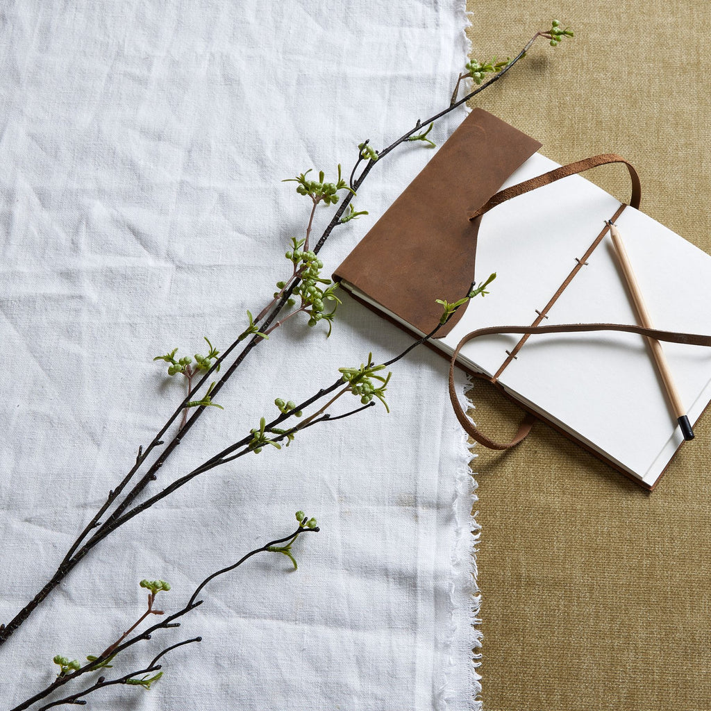 Artificial berry branches laid diagonally across white and tan fabric beside an open brown notebook and a pencil.