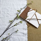 Artificial berry branches laid diagonally across white and tan fabric beside an open brown notebook and a pencil.