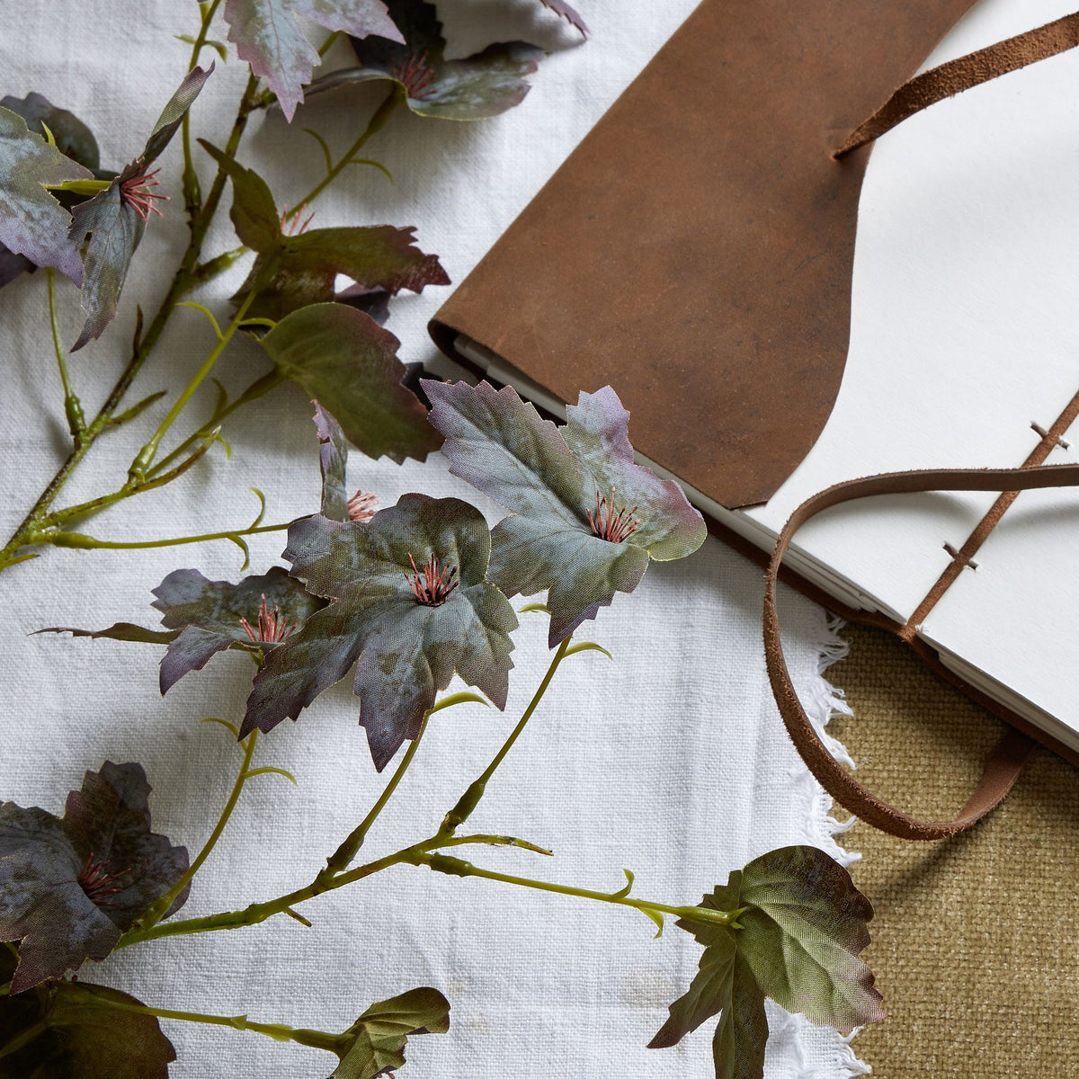 Close view of lobed artificial leaves with serrated edges, printed veining and dark-red radiating centres beside an open notebook.