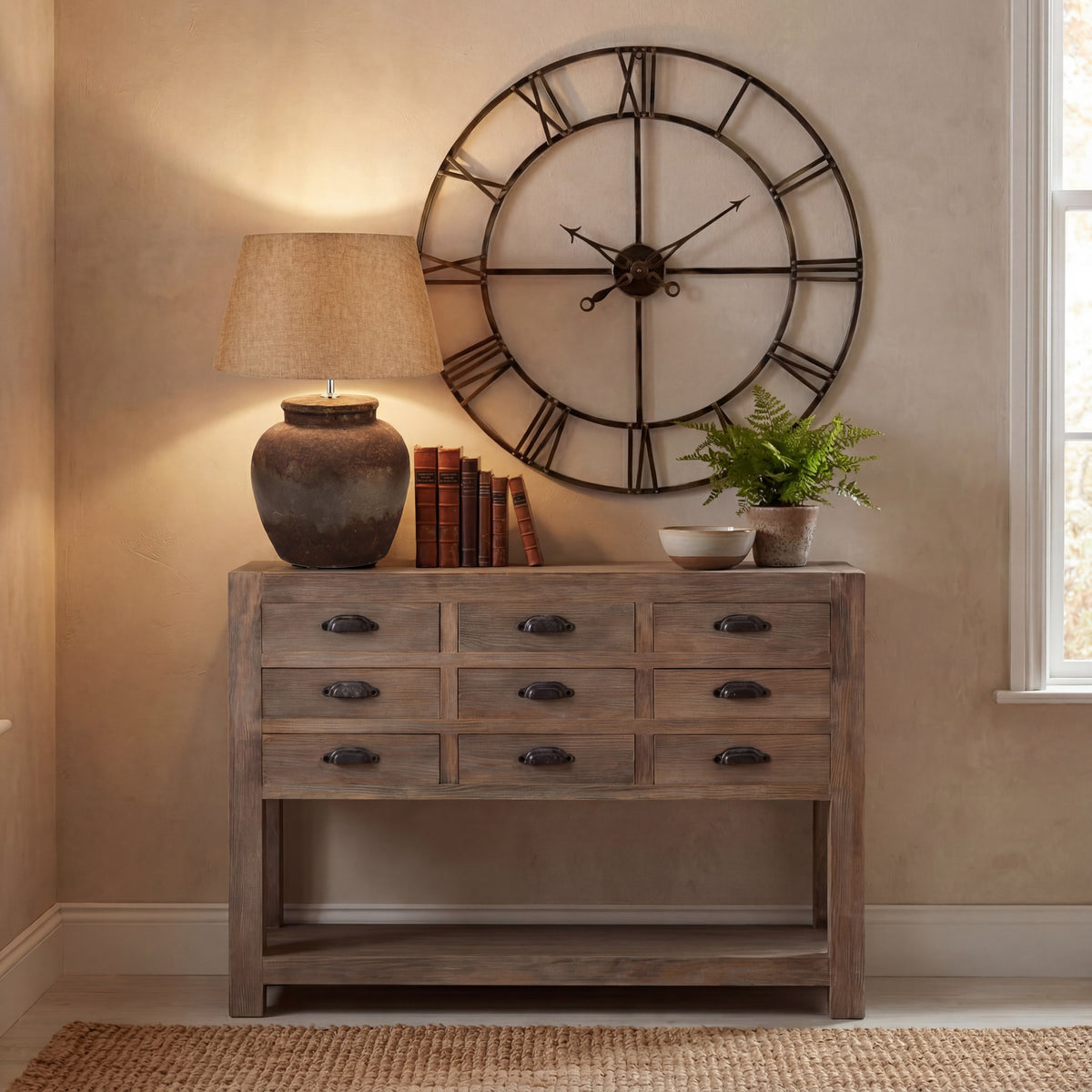 Mottled Pot Table Lamp pictured lit on a wooden console beside books, a bowl and a fern, beneath a large open-face wall clock.