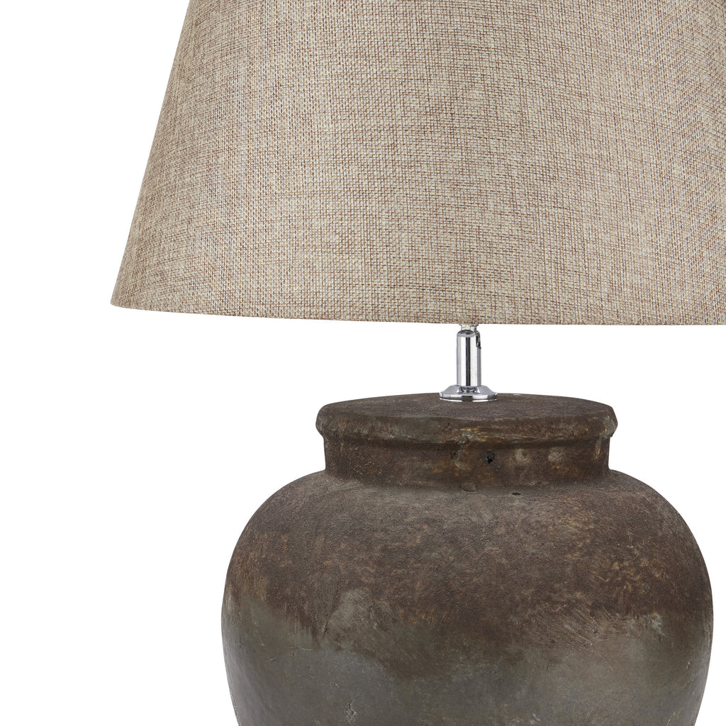 Close-up of the beige shade's weave-like texture above the broad pot lip and dark mottled surface of the lamp base.