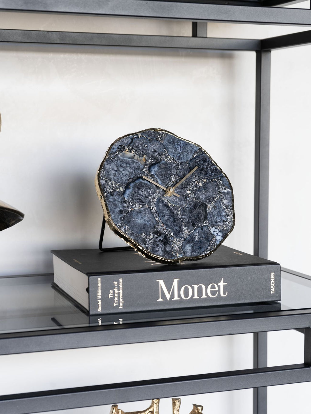 Smoky agate clock displayed on a Monet art book on a glass shelf with a black metal frame.