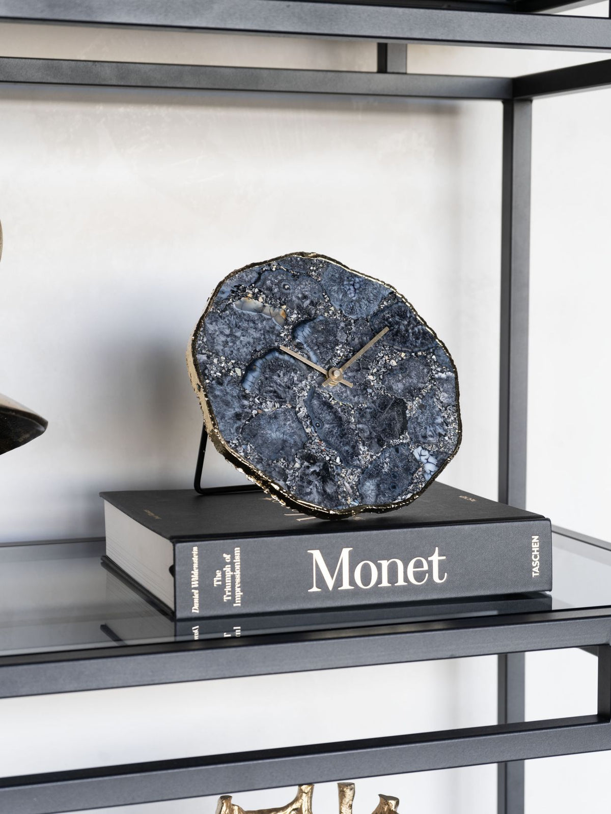 Smoky agate clock displayed on a Monet art book on a glass shelf with a black metal frame.
