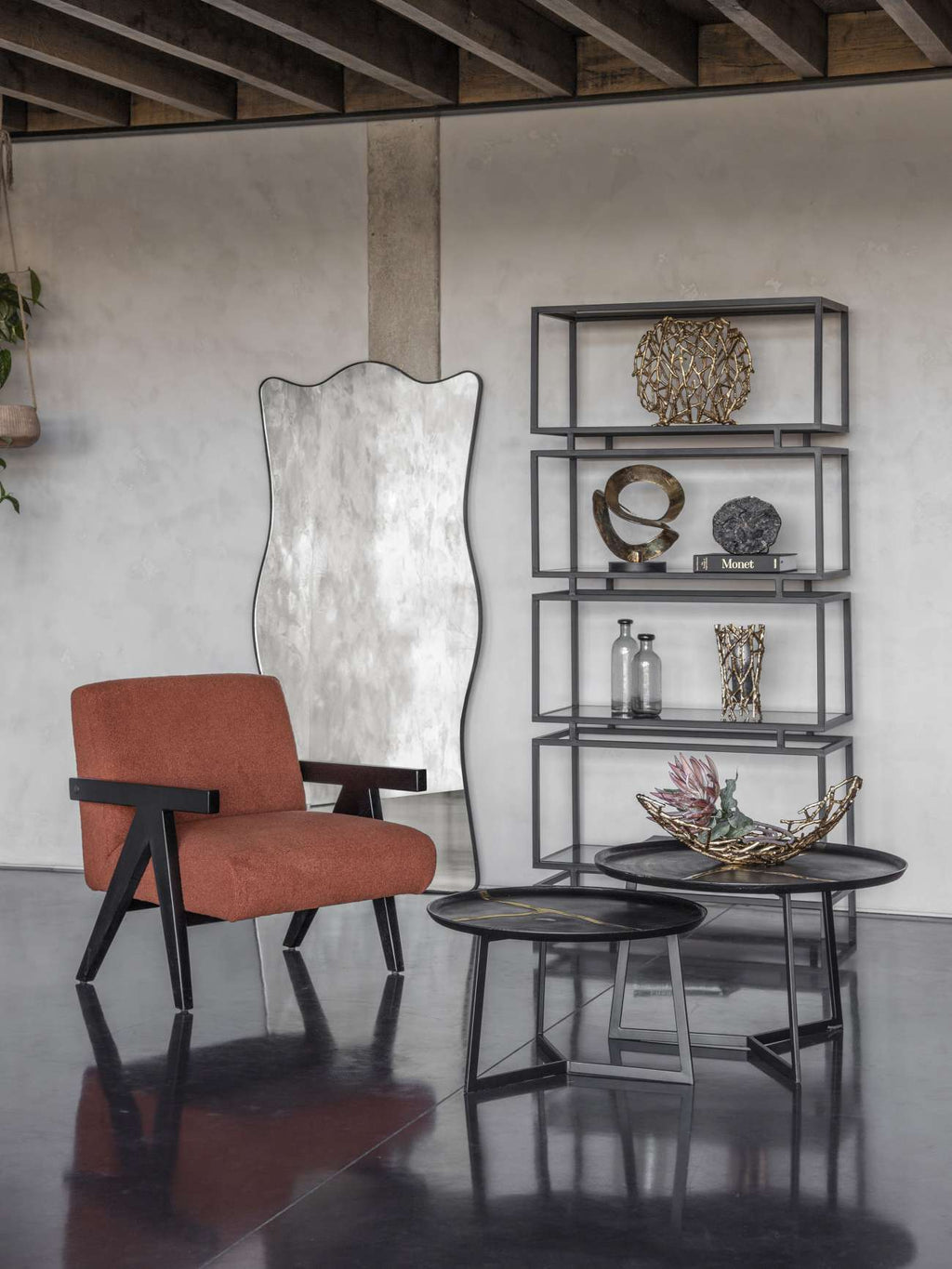 Agate clock on a book within black open shelving, beside a tall mirror, rust-coloured chair and round tables.