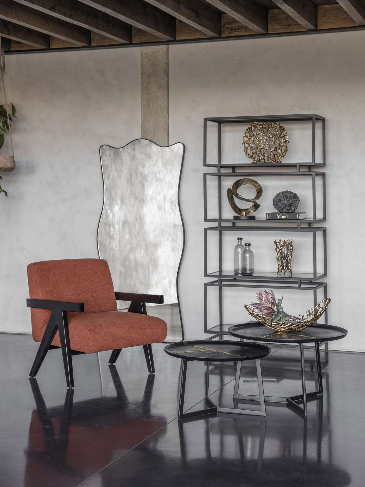 Agate clock on a book within black open shelving, beside a tall mirror, rust-coloured chair and round tables.