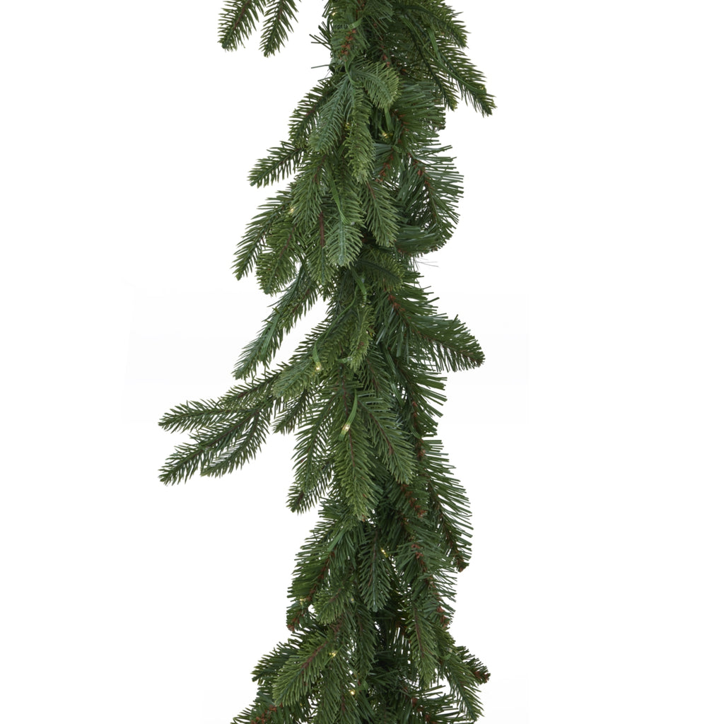 Close-up of the garland's overlapping green needle branches, showing longer projecting tips and small yellow points of light among the foliage.
