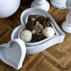 White heart-shaped dishes on a wooden tabletop, with two nested around pine cones and decorative balls and a smaller empty dish beside them.