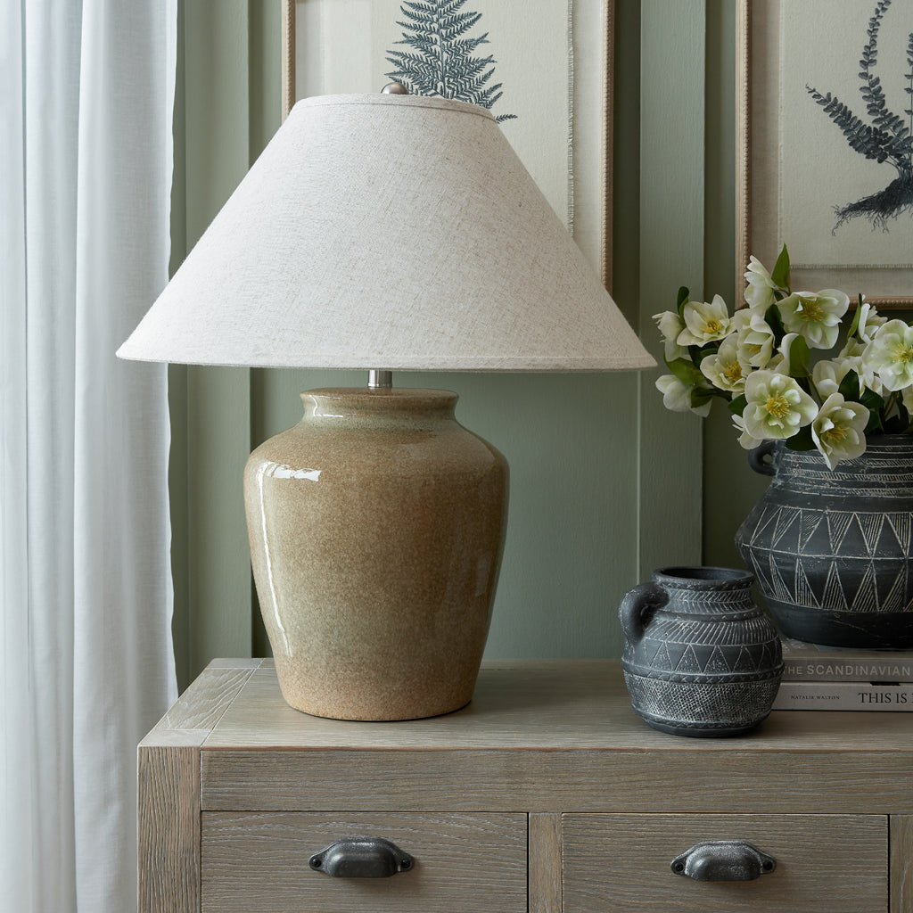 Olive Mottlejar Table Lamp on a wooden sideboard beside dark patterned vessels and white flowers, against green panelling and botanical pictures.