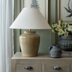 Olive Mottlejar Table Lamp on a wooden sideboard beside dark patterned vessels and white flowers, against green panelling and botanical pictures.