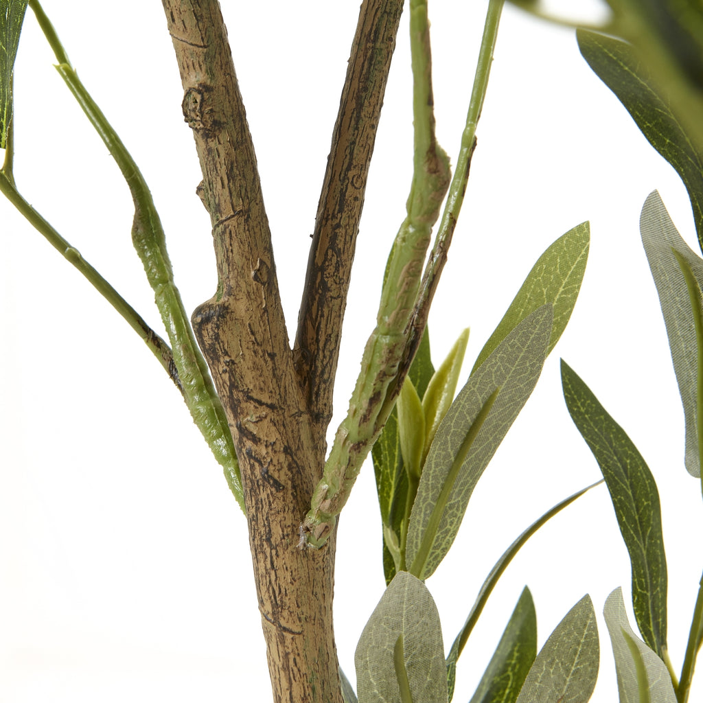 Detail of the mottled brown trunk where it forks, with slender green branches and narrow artificial leaves alongside.