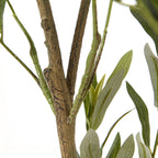 Detail of the mottled brown trunk where it forks, with slender green branches and narrow artificial leaves alongside.