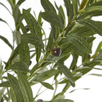 Close-up of pointed green artificial leaves with pale vein markings and a dark olive-like fruit on a slender branch.