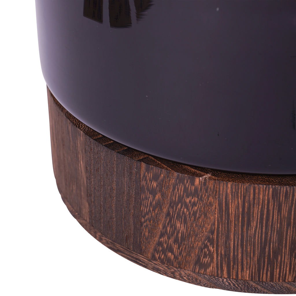 Close-up of the smooth black glass vase above its brown wooden base with visible grain.