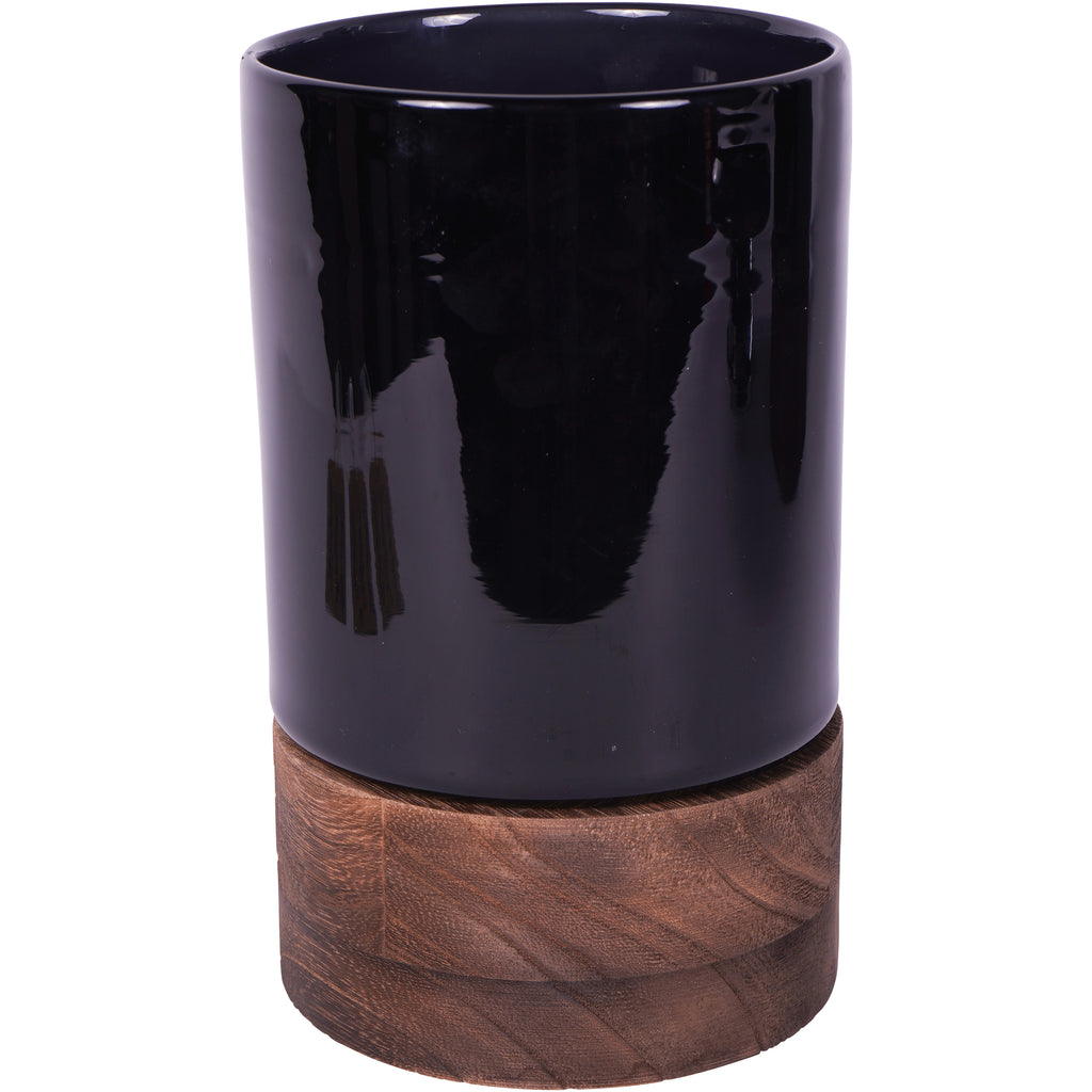 Opaque black cylindrical glass vessel on a brown wooden base, viewed from the front against white.