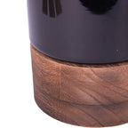Close-up of the black glass vessel resting on its brown wooden base, showing the wood grain.