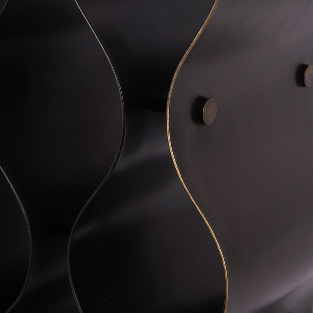 Close-up of the wine rack's dark metal surface, warm bronze-coloured curved edge and round connector end.