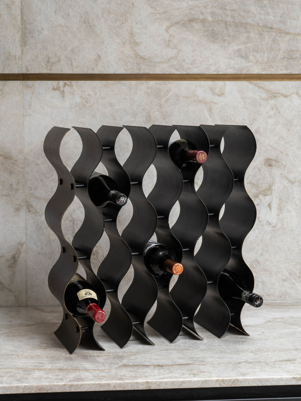 Upright wine rack holding five bottles on a pale stone counter against a matching stone wall.