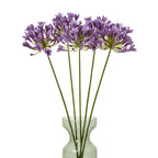 Several purple-lilac artificial flower stems spread across a translucent green vase against a white background.